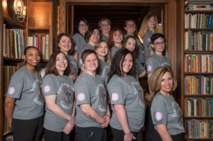 group of 14 women in grey t shirts with the maid for you logo that says transforming homes, changing lives